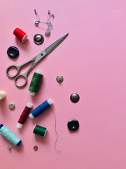 Scissors, threads, pins and buttons on a pink background