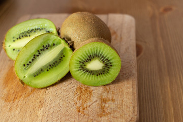 Whole and cut half of kiwi on wooden chopping board. Fresh juicy fruit, vegetarian product. Healthy organic food concept