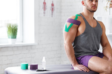 Kinesiology taping. Kinesiology tape on patient shoulder. Injured shoulder treatment of young male athlete. Post traumatic rehabilitation, sport physical therapy, recovery concept.