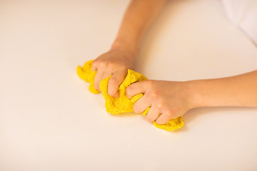 Obraz premium Girl's hands stretching yellow slime on white table