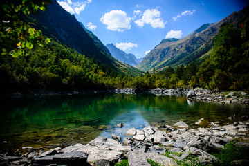 Сlear alpine lake against the blue sky. Green slopes of the mountains, stone shores.