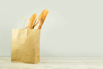 Two french baguette bread loafs in mockup plain paper bag on grey wooden table. Bakery and delivery...