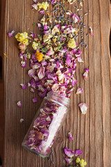 Opened glass bottle with dry mix of flowers on wooden background
