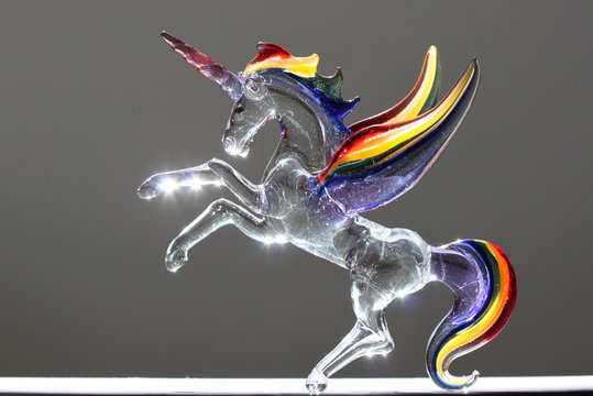 Reflet de soleil sur une licorne arc-en-ciel en cristal  avec  des ailes, une queue et une crini&egrave;re arc-en-ciel. La corne est iris&eacute;e et or.  Sun reflection on a crystal rainbow unicorn with wings.
