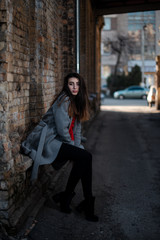 Girl in a red blouse and a gray cardigan on the background of the old brick wall