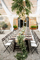 in backyard of villa in Tuscany there is banquet wooden table decorated with cotton and eucalyptus compositions, glasses, candles and plates are placed on table