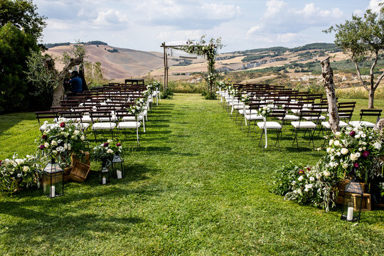 in backyard of villa in Tuscany there is banquet wooden table decorated with cotton and eucalyptus compositions, glasses, candles and plates are placed on table