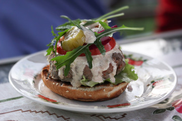 American cuisine. Fast food. Burger with beef, arugula, tomato, cucumber and sauce on a plate on the table. Summer picnic. Background image, copy space