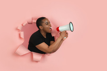 Shouting. Cheerful african-american young woman poses in torn coral paper background, emotional and...
