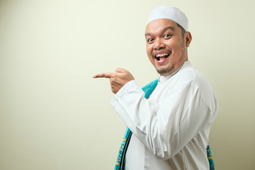 Portrait of Asian young muslim man smiling and pointing to presenting something on his side
