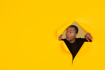 Wondered. Cheerful african-american young woman poses in torn yellow paper background, emotional and expressive. Breaking on, breakthrought. Concept of human emotions, facial expression, sales, ad.