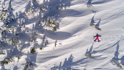 Top aerial view of young happy smiling girl making by arms snow angel figure and lying in snow,...