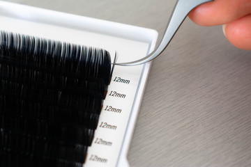 A beautician or lash artist picking up lashes with a pair of precision tweezers to make volume lashes fans for the beauty treatment; eyelash extensions