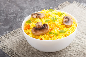 Yellow fried rice with champignons mushrooms, turmeric and oregano in white ceramic bowl on a black concrete background. side view.