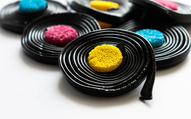 A close up of a collection of licorice sweets known as catherine wheels in the uk.  The main front sweetie has a yellow centre.  The confectionery sits on a white background.