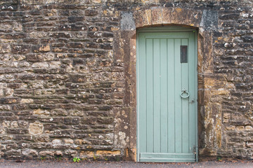 A stone wall with a light vintage green gate door to the right side of the frame.  The warm toned bricks and stone leave room in the image for text or copy.