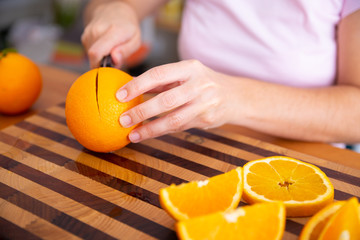 Lady holding knife and cutting orange on wooden board. Sliced citrus fruits. Orange laying on table. Cropped side view. Studio shot. Nutrition and vegetarian concept