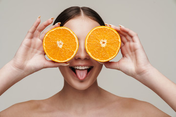 Image of cheerful shirtless woman smiling while making fun with orange