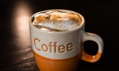 Close up of delicious cappuccino with cinnamon and milk foam in cup on dark table.