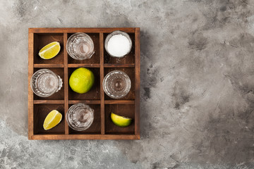 Tequila shots, limes and salt on wooden board on grey background. Top view, copy space