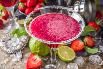 Summer cold alcohol drink. Strawberry margarita cocktail, with lime, mint and fresh strawberry on rustic wooden background