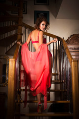 Brunette woman with curly hairstyle standing on a staircase in red underwear