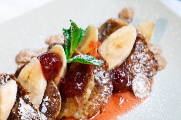 Juicy fritters with fruit for breakfast. Tasty cheesecakes with jam and bananas. Beautiful food from the restaurant cooked by a chef cook. Sweet dessert. A dish of flour and eggs.