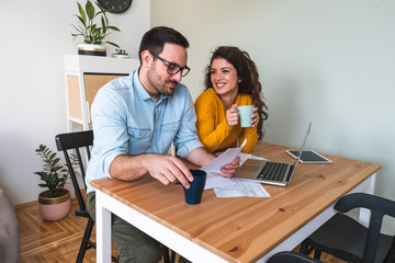 Smiling couple managing finances, reviewing their bank accounts using laptop computer and calculator at modern kitchen stock photo