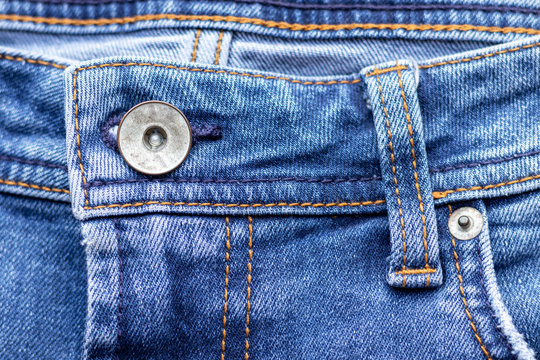 Jeans front with button and pocket. Bright blue denim fabric texture background. Closeup view