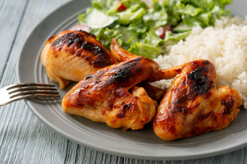 Grilled chicken wings and drumsticks, served with boiled rice and salad.