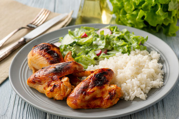 Grilled chicken wings and drumsticks, served with boiled rice and salad.