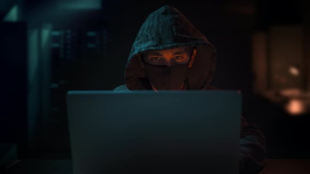 Hacker hooded and wearing mask coding on computer late night Hooded hacker stealing user data information 