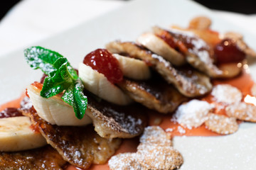 Juicy fritters with fruit for breakfast. Tasty cheesecakes with jam and bananas. Beautiful food from the restaurant cooked by a chef cook. Sweet dessert. A dish of flour and eggs.