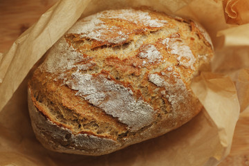 Freshly baked loaf of bread with flour covered crust unwrapped from baking paper