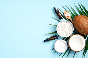 Flat lay composition with coconut oil cosmetics and tropical palm leaf on blue background. Top view...