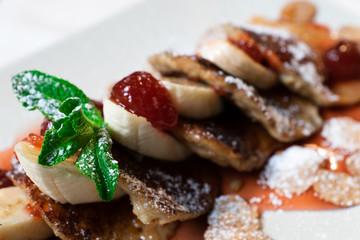 Juicy fritters with fruit for breakfast. Tasty cheesecakes with jam and bananas. Beautiful food from the restaurant cooked by a chef cook. Sweet dessert. A dish of flour and eggs.