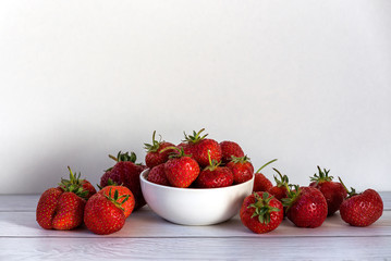 Heap of fresh strawberries in white ceramic bowl on rustic white wooden background
