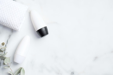 Roll-on deodorant packaging with eucalyptus leaf and towel on marble background. Flat lay, top view, copy space. Blank antiperspirant bottles mockups, sweat protection concept