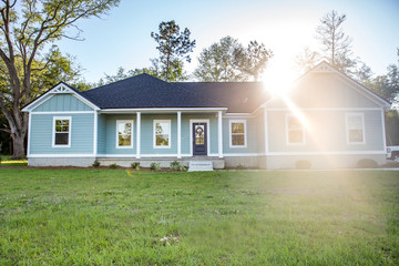 Fototapeta na wymiar Front view of a brand new construction house with blue siding, a ranch style home with a yard and a sunflare