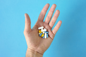 A handful of multicolored tablets and vitamins in a man's hand on a blue background. above. Close-up. place for sign