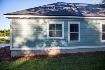 rear view of a brand new construction house with blue siding, a ranch style home with a yard on a...