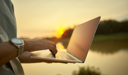 Close-up of a young man using a laptop and the lake and nature at sunset
