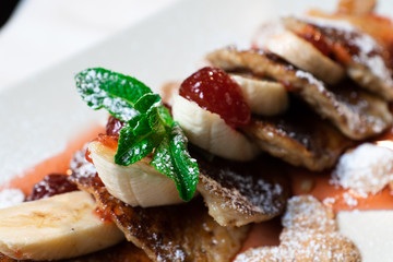 Juicy fritters with fruit for breakfast. Tasty cheesecakes with jam and bananas. Beautiful food from the restaurant cooked by a chef cook. Sweet dessert. A dish of flour and eggs.