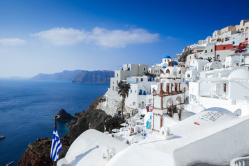 Panorama of Oia village, bell tower, Greek flag cliffs with the aegean sea, Santorini island, Cyclades Greece