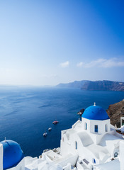 Fototapeta na wymiar Panorama from Oia, blue domes of orthodox church and the caldera with boats in the back, Santorini island, Cyclades, Greece