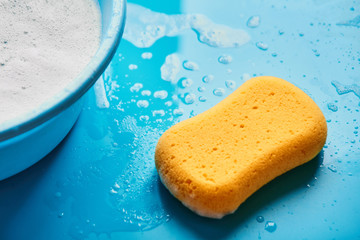 Yellow washing sponge in soap foam on a blue background isolated