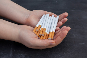 The girl holds a lot of loose cigarettes in her hands. Black background