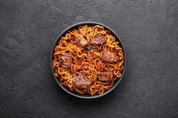 Ram-Don or Chapaguri noodles with beef steak in black bowl on dark slate background. Jjapaguri is a popular south korean dish with ramen and udon noodles and beef steak.