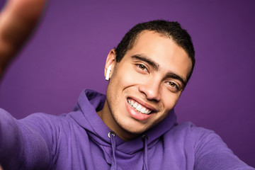 Obraz premium Young funny energetic man doing selfie and smiling. Look from phone. Isolated over purple background. Camera view