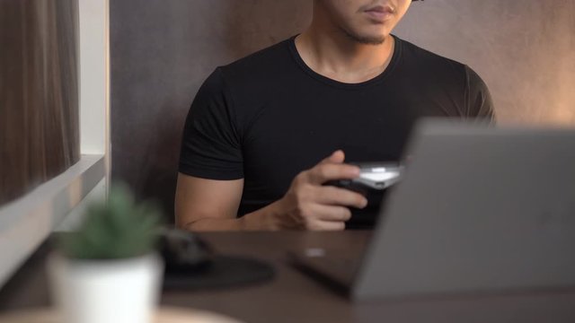 Asian man Gaming by using joy controller and laptop at home, hobby, technology and leisure time concept, Excited gamer holding joystick, home quarantine lifestyle during covid-19 pandemic, e-sports